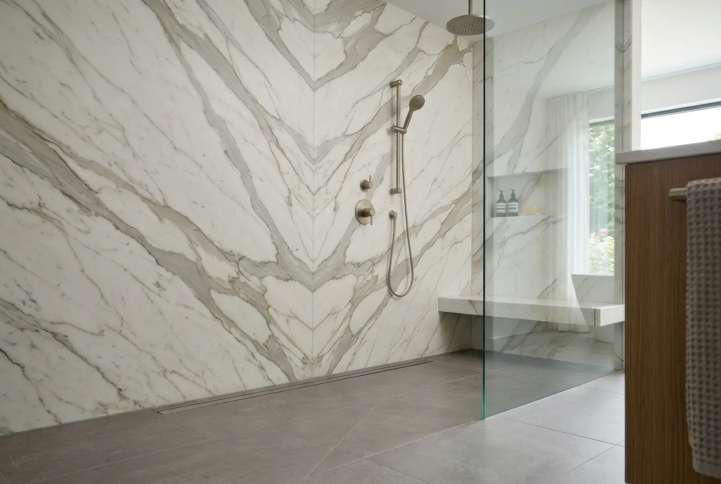 Bookmatched Calacatta marble shower wall with mirror-image veining and a linear drain