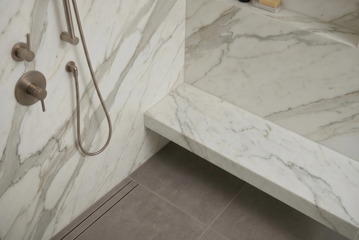 Detail of brushed nickel shower controls, handheld, and a floating Calacatta marble bench
