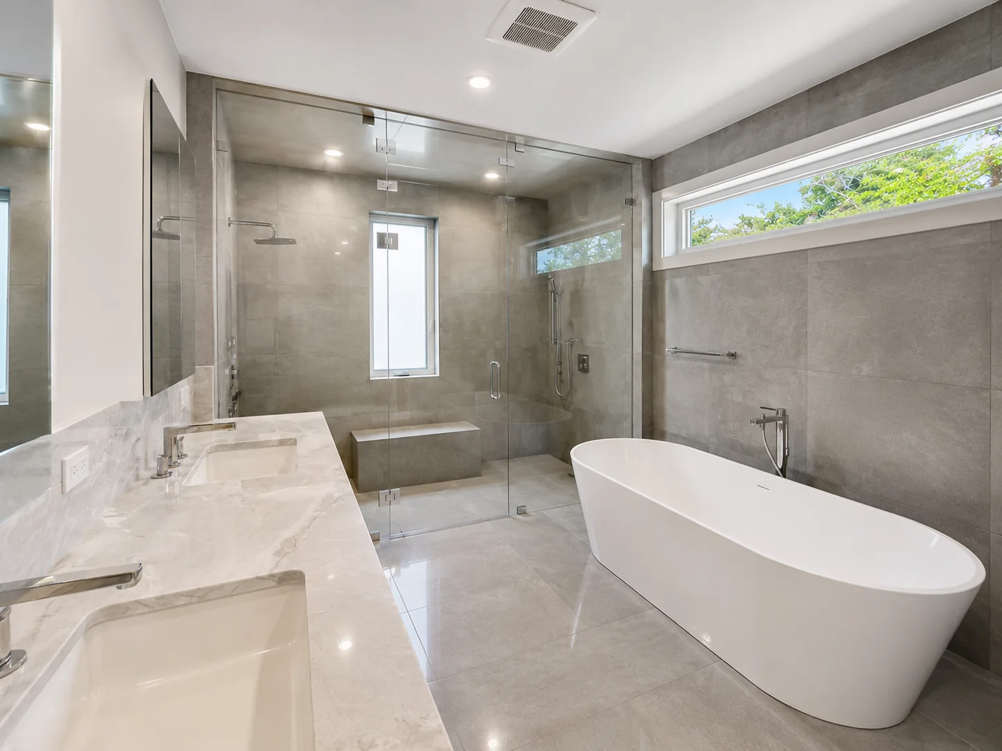 Large-format gray bathroom tile with freestanding tub, double vanity, and shower